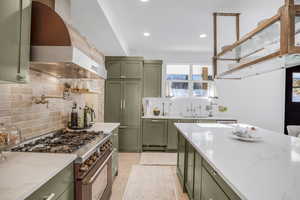 Kitchen with high end range, wall chimney exhaust hood, a sink, and green cabinetry