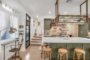 Kitchen featuring green cabinetry, visible vents, light stone counters, and tasteful backsplash