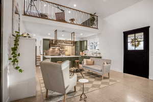 Living room with light speckled floor, a towering ceiling, and a healthy amount of sunlight