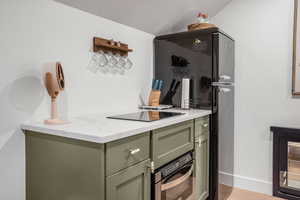 Interior space featuring green cabinets, wood finished floors, black electric stovetop, baseboards, and oven