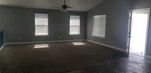 Spare room featuring lofted ceiling, baseboards, a ceiling fan, dark stone finish flooring, and dark colored carpet