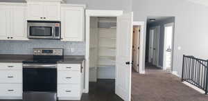 Kitchen with appliances with stainless steel finishes, dark countertops, tasteful backsplash, and white cabinetry