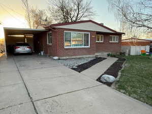 Property exterior at dusk with concrete driveway, fence, brick siding, and carport