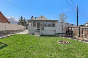 Back of house featuring a lawn, a fenced backyard, a sunroom, and an outdoor fire pit
