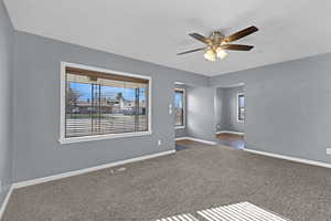 Unfurnished room featuring dark carpet, baseboards, a ceiling fan, and visible vents
