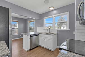 Kitchen with a peninsula, white cabinets, stainless steel appliances, light wood finished floors, and a sink