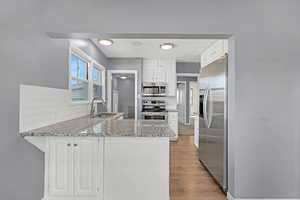 Kitchen with tasteful backsplash, a peninsula, light stone countertops, appliances with stainless steel finishes, and a sink