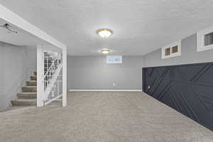 Basement featuring baseboards, a textured ceiling, carpet flooring, and stairs