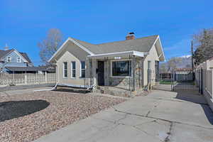 Bungalow-style house with stucco siding, a chimney, a gate, fence, and a shingled roof
