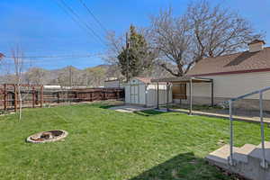 View of yard featuring a shed, an outbuilding, a fenced backyard, and an outdoor fire pit