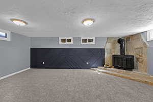 Unfurnished living room featuring a wood stove, carpet flooring, baseboards, and a textured ceiling