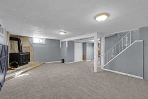 Below grade area featuring a wood stove, carpet flooring, a textured ceiling, and stairs