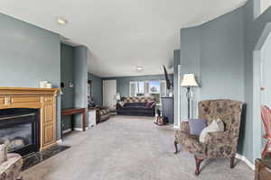 Carpeted living area featuring a fireplace with flush hearth and baseboards