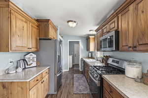 Kitchen featuring brown cabinetry, stainless steel appliances, light countertops, washer / clothes dryer, and dark wood-style floors