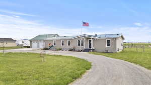 View of front of property featuring a front lawn, metal roof, fence, an attached garage, and dirt driveway