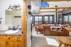 Living room with carpet flooring, plenty of natural light, vaulted ceiling with beams, and a wood stove
