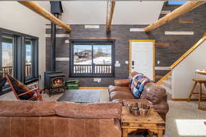 Living area featuring stairway, a wood stove, carpet, beamed ceiling, and a wealth of natural light