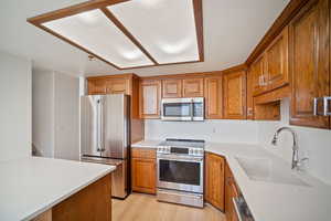 Kitchen featuring light wood finished floors, stainless steel appliances, light countertops, a sink, and brown cabinetry