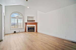 Family room featuring wood finished floors, a glass covered fireplace, baseboards, lofted ceiling, and visible vents
