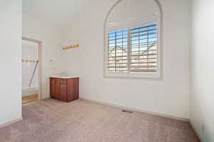 Primary bedroom featuring lofted ceiling, light carpet, and baseboards.