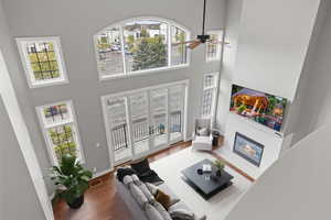 Living area featuring ceiling fan, a wealth of natural light, a towering ceiling, a glass covered fireplace, and wood finished floors