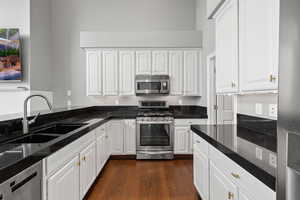 Kitchen featuring appliances with stainless steel finishes, white cabinetry, dark stone counters, dark wood finished floors, and a sink