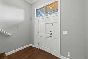 Foyer featuring dark wood-type flooring, ornamental molding, and baseboards