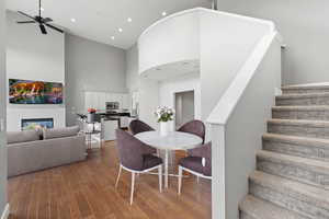 Dining space with a high ceiling, a ceiling fan, hardwood / wood-style flooring, stairs, and a glass covered fireplace