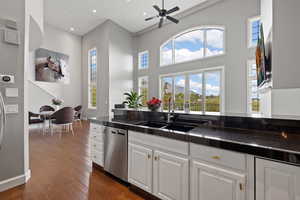 Kitchen with white cabinets, dishwasher, a sink, dark wood-style flooring, and dark countertops