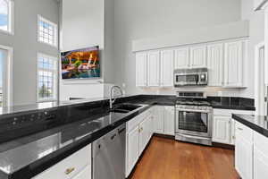 Kitchen featuring dark wood-style flooring, a high ceiling, white cabinets, appliances with stainless steel finishes, and a sink