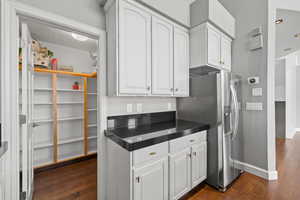Kitchen featuring white cabinets, dark countertops, stainless steel fridge, and dark wood-style floors