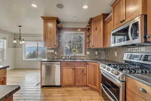 Kitchen featuring open shelves, a large sink, upgraded countertops, light wood-style floors, and stainless steel appliances