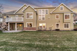 Back of property with board and batten siding, a wooden deck, a patio, and a lawn