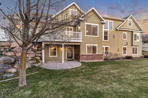 Back of property with board and batten siding, brick siding, a lawn, and a patio area