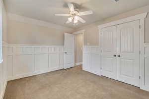 Bedroom featuring a closet, a wainscoted wall, ceiling fan, a decorative wall, and light colored carpet