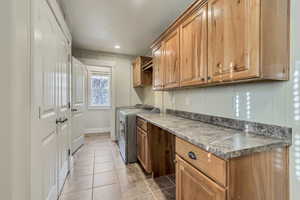 Laundry room, light tile patterned floors, washing machine and dryer, and lots of cabinet space