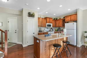 Kitchen featuring a sink, brown cabinetry, white appliances, and dark wood-style floors