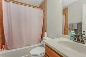 Bathroom featuring toilet, shower / bathtub combination with curtain, and vanity