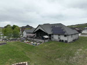 Back of house featuring a shingled roof, solar panels, a lawn, and a garden