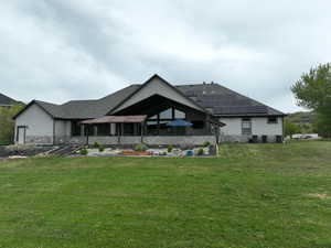 Back of property with a lawn, a shingled roof, and stone siding