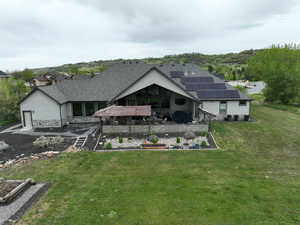 Rear view of property with a deck, a yard, a shingled roof, solar panels, and a vegetable garden