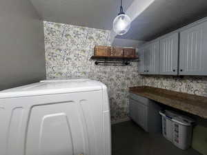 Laundry room featuring washer / clothes dryer, dark tile patterned floors, wallpapered walls, baseboards, and cabinet space