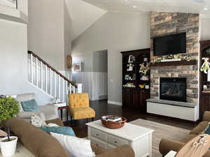 Living area with wood finished floors, high vaulted ceiling, a fireplace, and stairway
