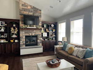 Living room featuring a textured ceiling, a stone fireplace, dark wood finished floors, and vaulted ceiling