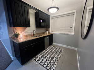 Kitchen with light tile patterned floors, baseboards, dishwasher, a sink, and dark cabinets