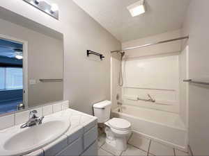 Bathroom featuring toilet,  shower combination, a textured ceiling, vanity, and tile patterned flooring
