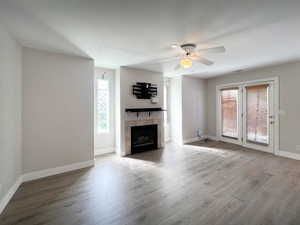 Unfurnished living room featuring wood finished floors, ceiling fan, a tiled fireplace, and baseboards
