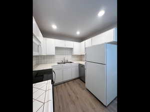 Kitchen with white cabinets, a sink, white appliances, light wood finished floors, and tile countertops