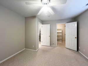 Unfurnished bedroom featuring baseboards, a walk in closet, visible vents, ceiling fan, and light colored carpet