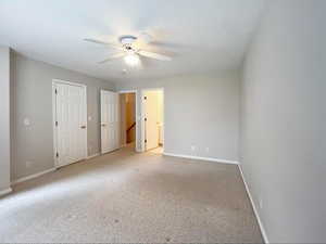 Unfurnished bedroom featuring ensuite bathroom, light colored carpet, baseboards, and a ceiling fan